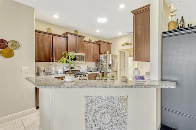 kitchen featuring light stone counters, brown cabinetry, a peninsula, and stainless steel appliances