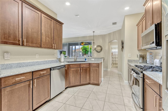 kitchen with a peninsula, arched walkways, light stone counters, a sink, and stainless steel appliances