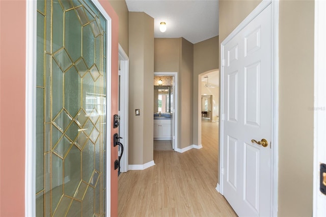 foyer entrance featuring light wood-style floors, arched walkways, and baseboards