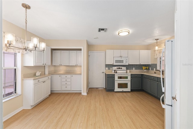 kitchen with gray cabinetry, light wood finished floors, white appliances, and visible vents