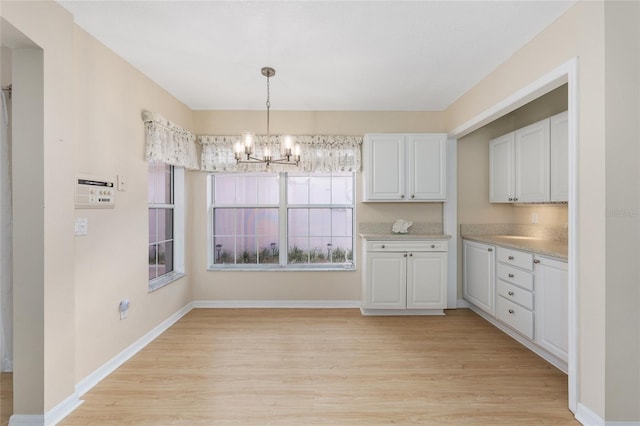 unfurnished dining area featuring baseboards, light wood-type flooring, and a chandelier