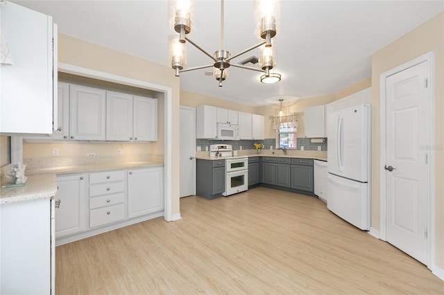 kitchen with an inviting chandelier, white appliances, tasteful backsplash, light wood-style flooring, and gray cabinetry