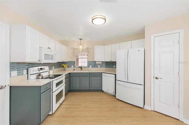 kitchen featuring tasteful backsplash, a sink, gray cabinetry, white cabinets, and white appliances