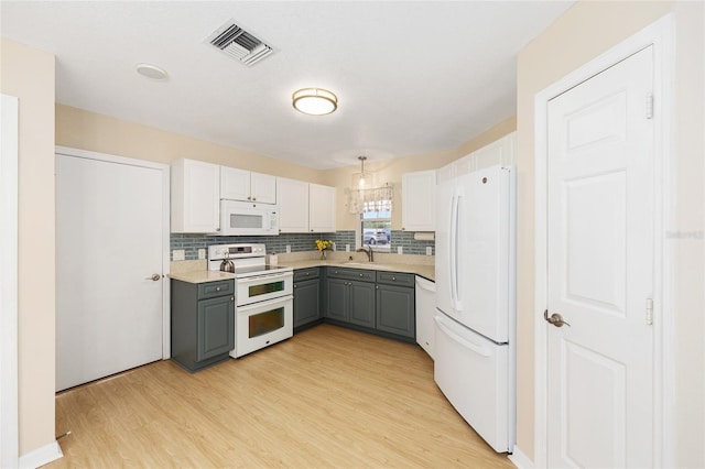 kitchen featuring visible vents, tasteful backsplash, gray cabinetry, a sink, and white appliances