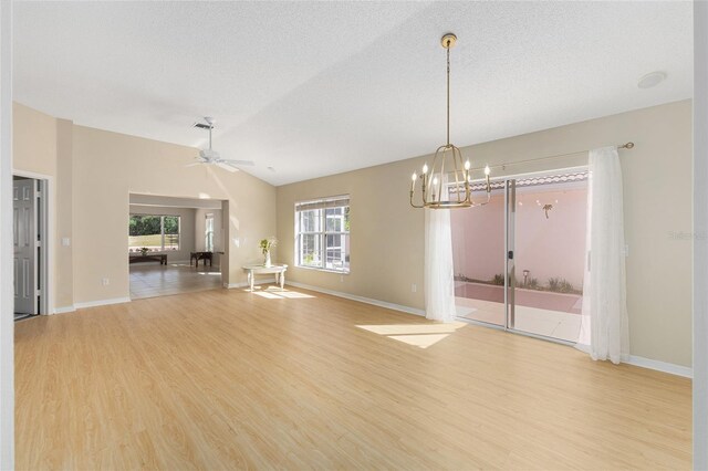 spare room featuring light wood-style floors, a textured ceiling, ceiling fan with notable chandelier, baseboards, and vaulted ceiling