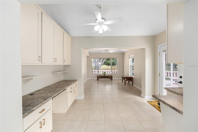 interior space with baseboards, white cabinetry, ceiling fan, and light tile patterned floors