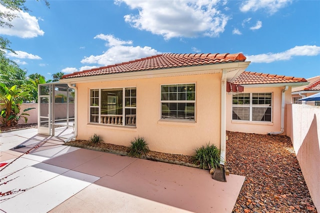 view of side of property featuring fence, a patio, stucco siding, and a tile roof