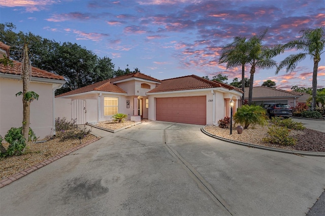 mediterranean / spanish-style home featuring a garage, stucco siding, a tiled roof, and concrete driveway
