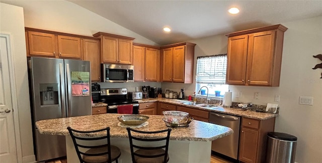 kitchen with a breakfast bar area, brown cabinetry, a sink, lofted ceiling, and stainless steel appliances