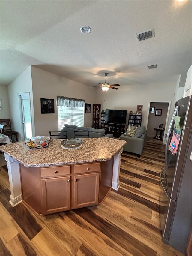 kitchen featuring visible vents, freestanding refrigerator, open floor plan, dark wood-style floors, and a center island