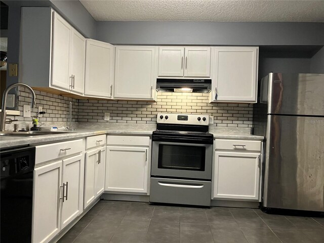 kitchen featuring dark tile patterned floors, white cabinetry, under cabinet range hood, a sink, and appliances with stainless steel finishes