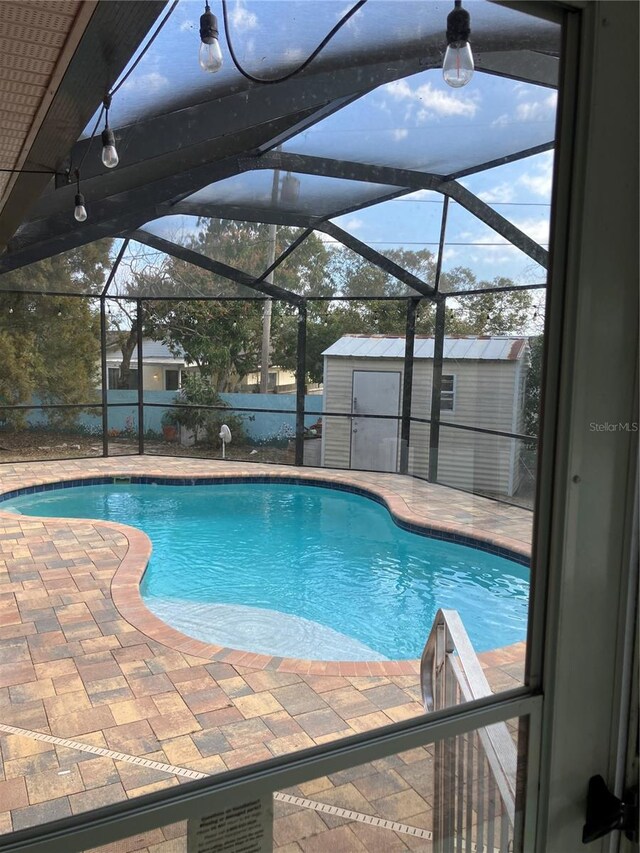 pool with a storage unit, glass enclosure, an outbuilding, and a patio