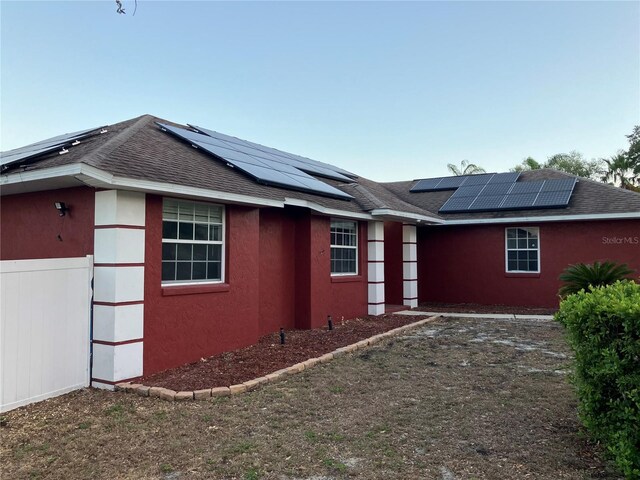 view of side of home featuring roof with shingles, stucco siding, and solar panels