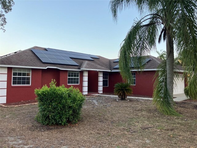 single story home with roof with shingles, stucco siding, roof mounted solar panels, and a garage