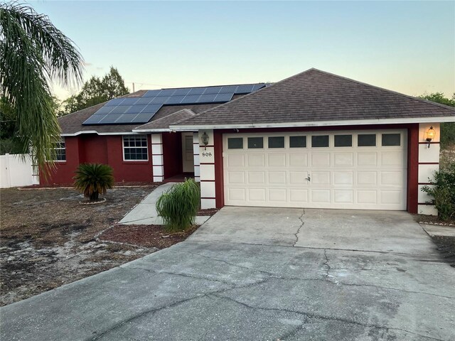 single story home featuring solar panels, a garage, roof with shingles, and concrete driveway