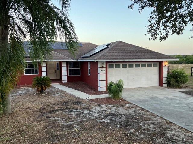 ranch-style home with roof with shingles, stucco siding, roof mounted solar panels, an attached garage, and driveway
