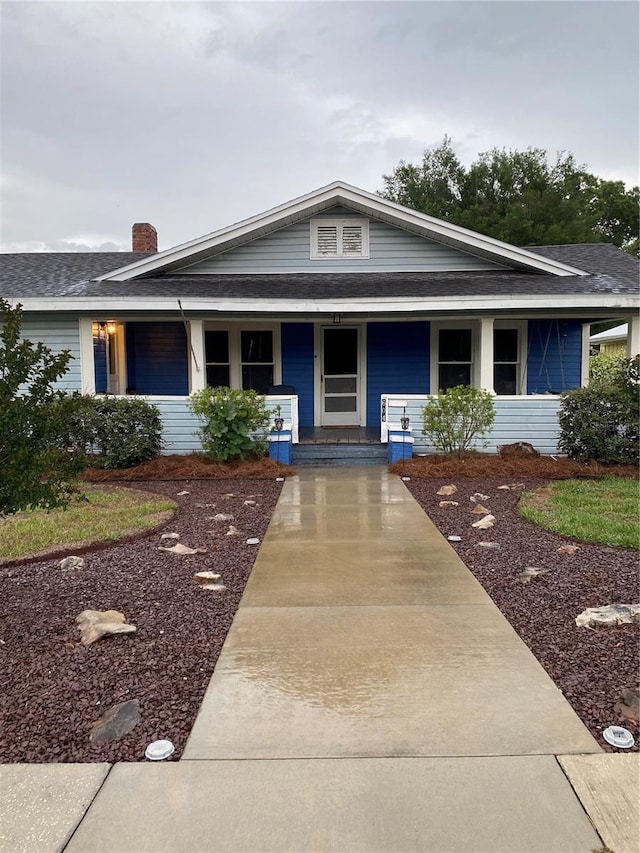 view of front of home featuring roof with shingles, a chimney, and a porch