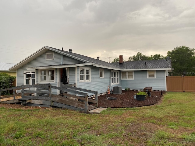 rear view of property featuring a chimney, a lawn, a wooden deck, central AC unit, and fence