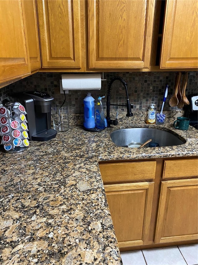interior space featuring brown cabinets, a sink, dark stone counters, decorative backsplash, and light tile patterned floors