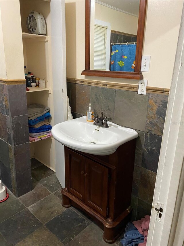 full bath with wainscoting, tile walls, stone finish floor, and vanity