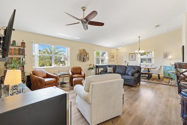 living area featuring light wood-style flooring, ceiling fan with notable chandelier, and lofted ceiling