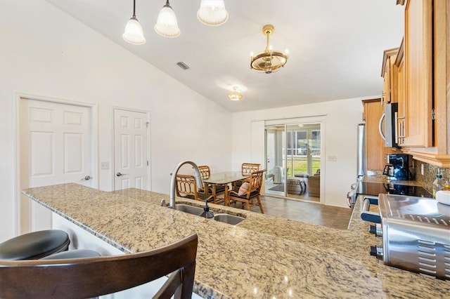 kitchen with brown cabinetry, visible vents, a sink, stainless steel microwave, and a breakfast bar