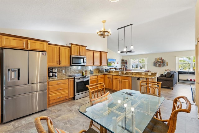 kitchen featuring brown cabinetry, a sink, a peninsula, an inviting chandelier, and stainless steel appliances