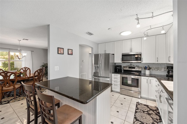 kitchen with appliances with stainless steel finishes, arched walkways, white cabinetry, light tile patterned floors, and visible vents