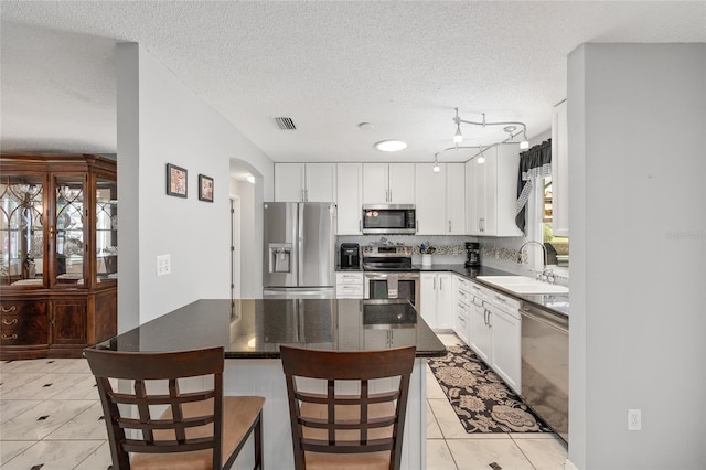 kitchen featuring a sink, appliances with stainless steel finishes, dark countertops, and a textured ceiling