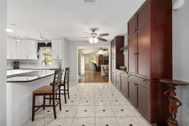 kitchen with a sink, a breakfast bar area, a ceiling fan, and a textured ceiling