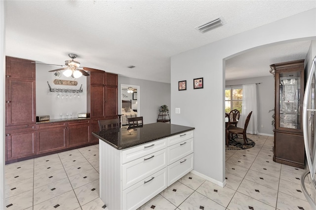 kitchen featuring visible vents, a ceiling fan, a textured ceiling, arched walkways, and dark stone countertops