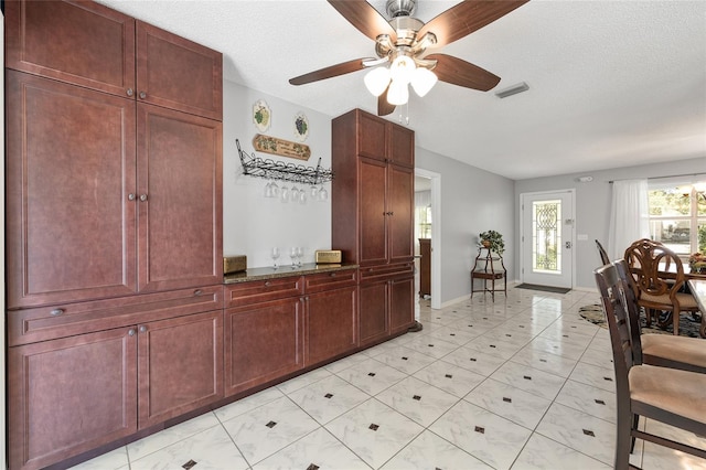 interior space featuring ceiling fan, visible vents, light tile patterned floors, baseboards, and reddish brown cabinets