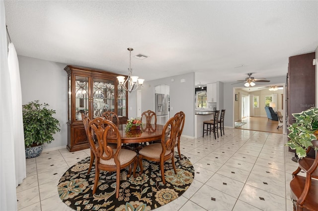 dining space featuring visible vents, baseboards, a textured ceiling, ceiling fan with notable chandelier, and light tile patterned floors