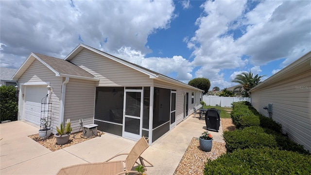 exterior space featuring fence, driveway, a sunroom, and a garage