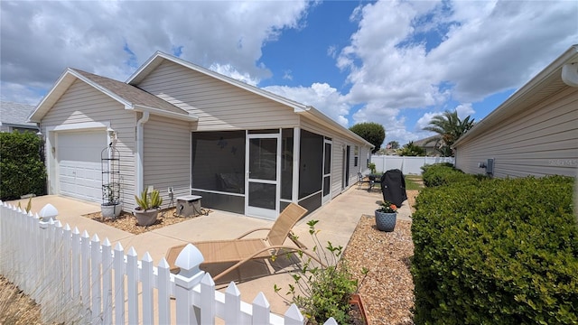 back of property with a garage, a sunroom, a fenced backyard, and a patio area