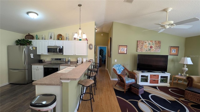 kitchen featuring open floor plan, a breakfast bar area, a sink, appliances with stainless steel finishes, and vaulted ceiling