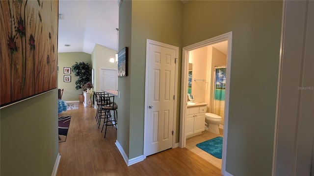 corridor featuring baseboards, lofted ceiling, and light wood finished floors