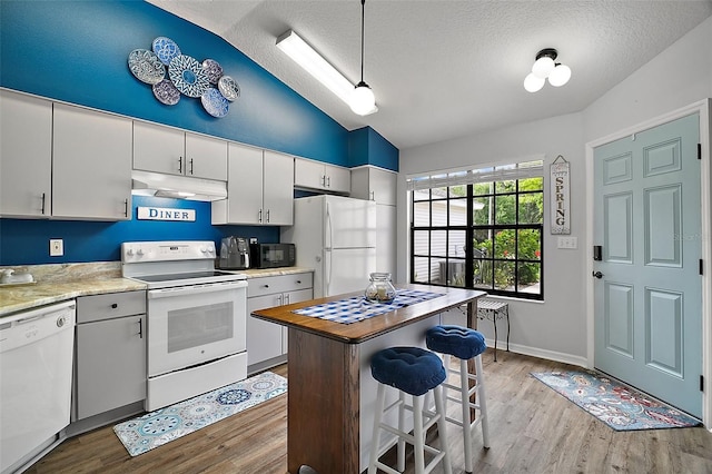 kitchen with vaulted ceiling, under cabinet range hood, white appliances, and wood finished floors