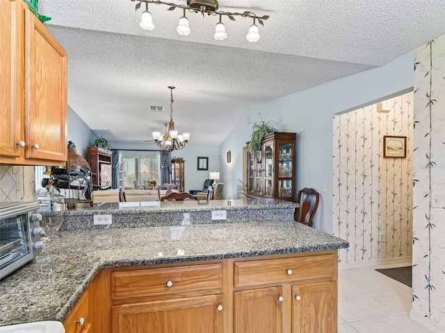 kitchen with a notable chandelier, a peninsula, light tile patterned floors, lofted ceiling, and visible vents