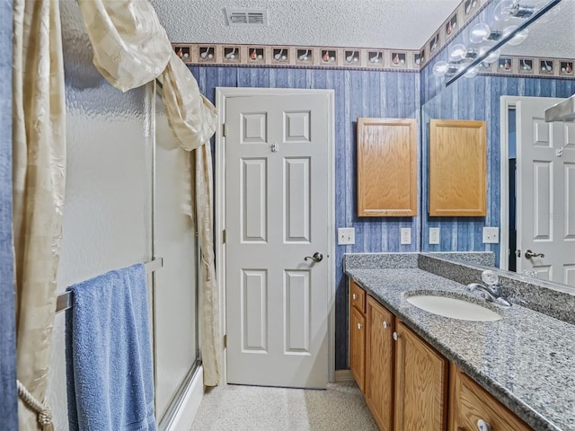 bathroom with visible vents, vanity, wallpapered walls, a textured ceiling, and a shower stall