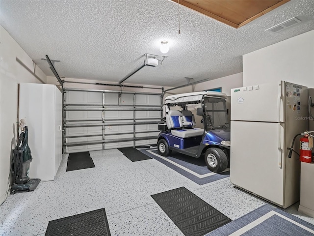 garage with a garage door opener, freestanding refrigerator, and visible vents