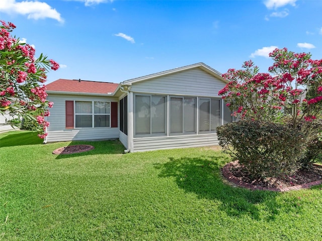 back of property with a lawn, a shingled roof, and a sunroom