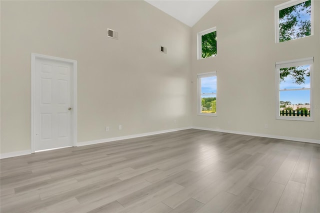 spare room with baseboards, light wood finished floors, visible vents, and high vaulted ceiling