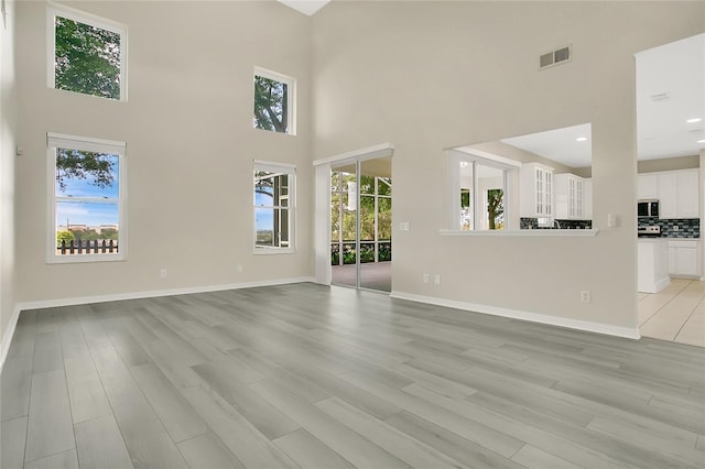 unfurnished living room with baseboards, light wood-style floors, visible vents, and a high ceiling