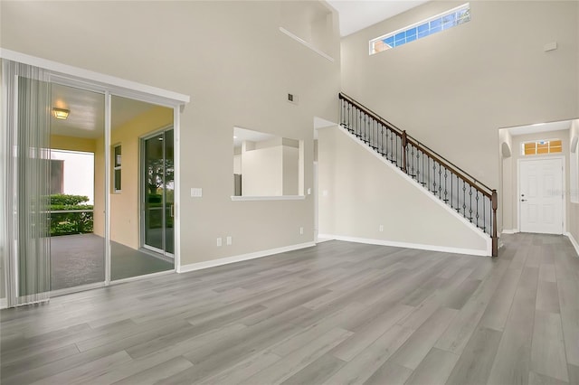 unfurnished living room featuring visible vents, wood finished floors, a towering ceiling, and stairs