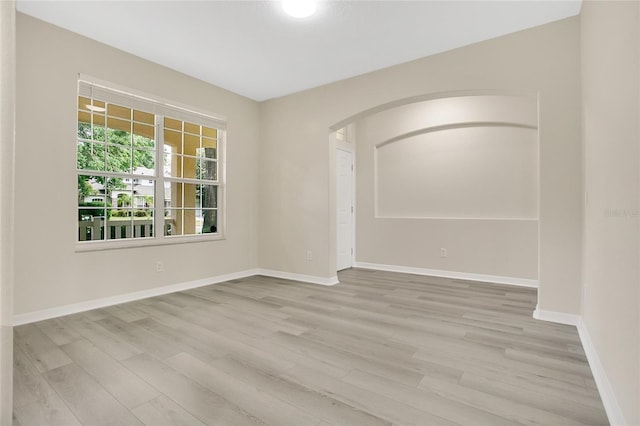 empty room featuring arched walkways, baseboards, and light wood-style flooring