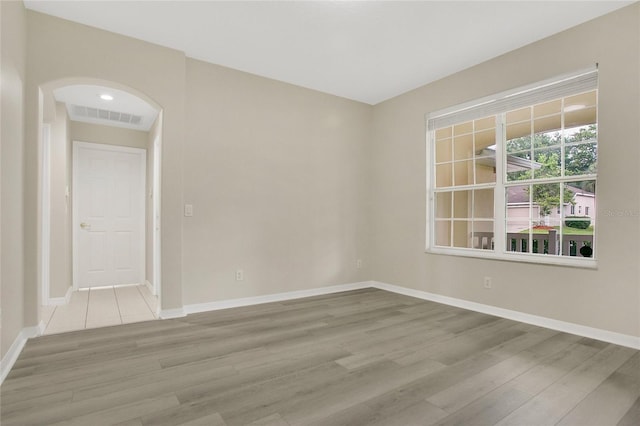 unfurnished room featuring visible vents, wood finished floors, baseboards, and arched walkways