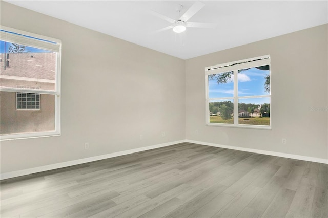 empty room with baseboards, a ceiling fan, plenty of natural light, and wood finished floors
