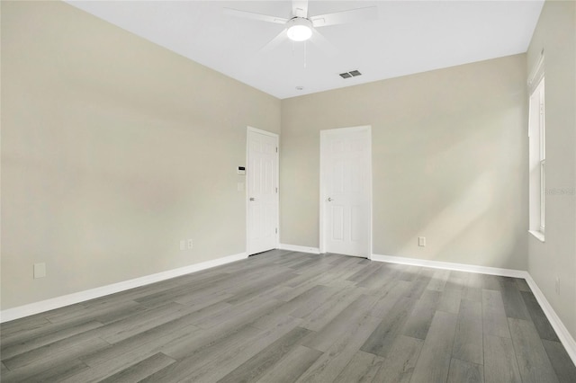 unfurnished room featuring baseboards, visible vents, wood finished floors, and a ceiling fan