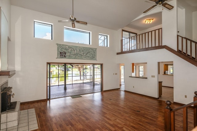 unfurnished living room featuring ceiling fan, a tiled fireplace, and a towering ceiling